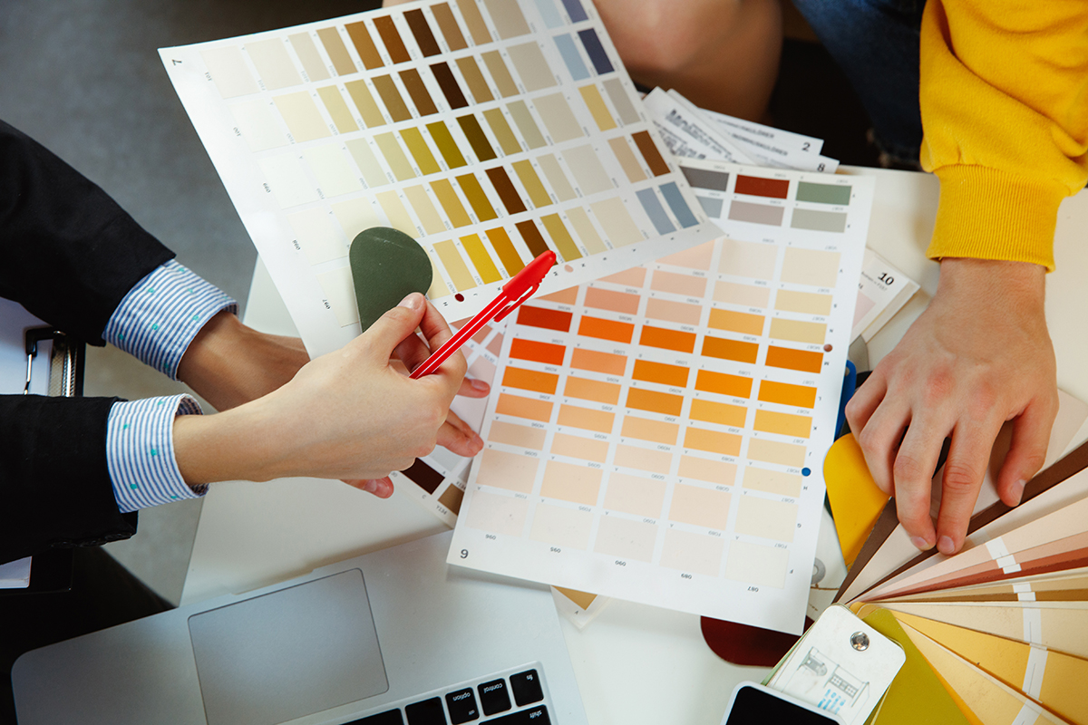 Interior designer working with young couple. Lovely family and professional designer or architector discussing conept of future interior, working with colour palette, room drawings in modern office.